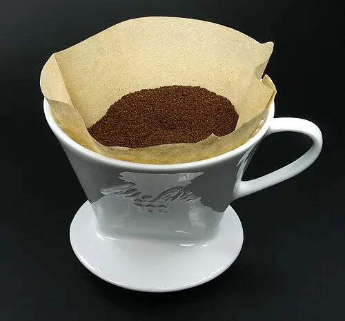 Weißer Melitta-102-Handfilter mit Papierfilter und gemahlenem Kaffee.
