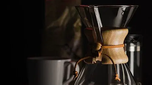 Chemex-Glaskaraffe mit Holzmanschette neben einer Tasse.
