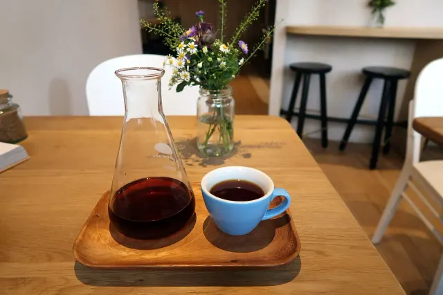 Schmale Glaskaraffe mit Kaffee neben einer blauen Tasse auf einem Tablett.