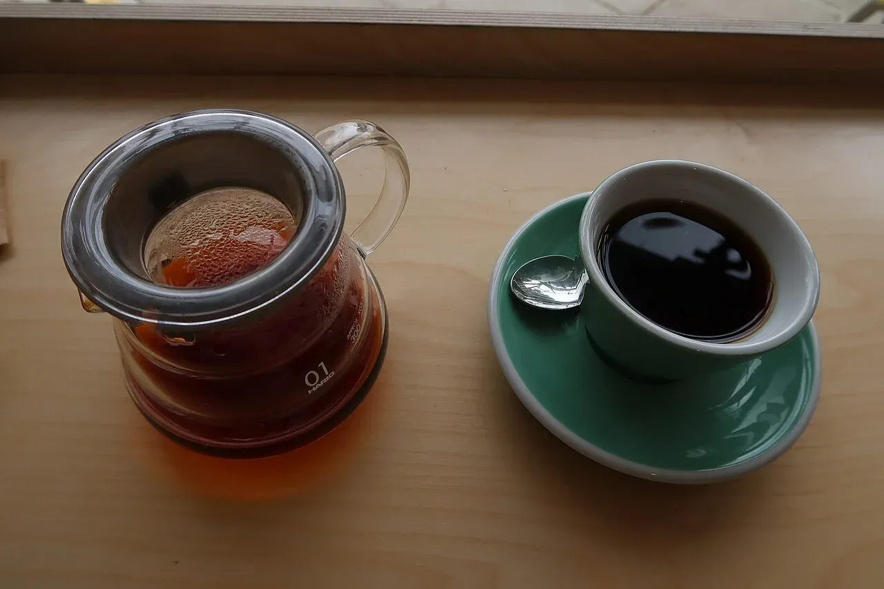 Kaffee im Glasserver mit Henkel neben einer grünen Tasse.