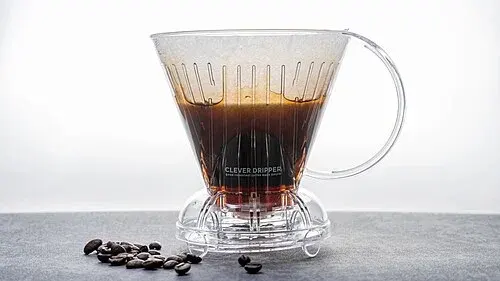 Transparenter Clever Dripper mit Filterpapier und ziehendem Kaffee auf einer freien Arbeitsfläche.