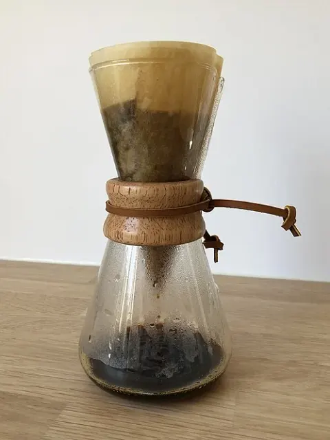 Chemex-Glaskaraffe mit Holzmanschette und eingesetztem Papierfilter mit Kaffeemehl.