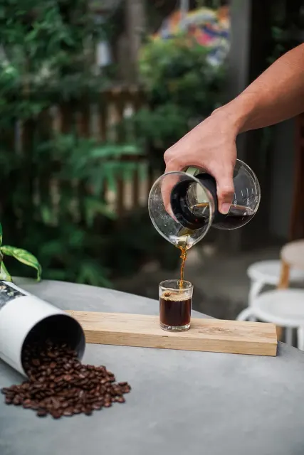 Kalter Kaffee wird aus einer Glaskanne in ein kleines Glas mit Eis gegossen.