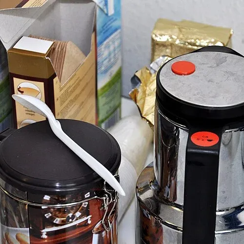 Isolierkanne mit schwarzem Deckel neben Kaffeedose, Löffel und Papierfiltern.