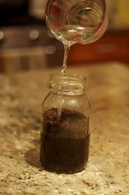 Wasser aus einem gläsernen Messbecher wird für Cold Brew in ein Einmachglas mit gemahlenem Kaffee gegossen.