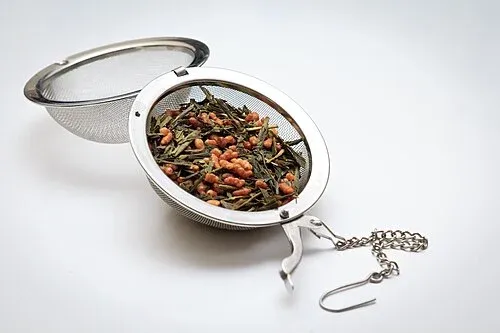 Geöffnetes feinmaschiges Metall-Teesieb mit Genmaicha-Blättern und geröstetem Reis.