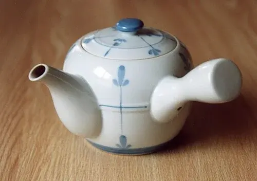 Weiße Kyūsu mit blauem Pflanzendekor, seitlichem Griff und Deckel.
