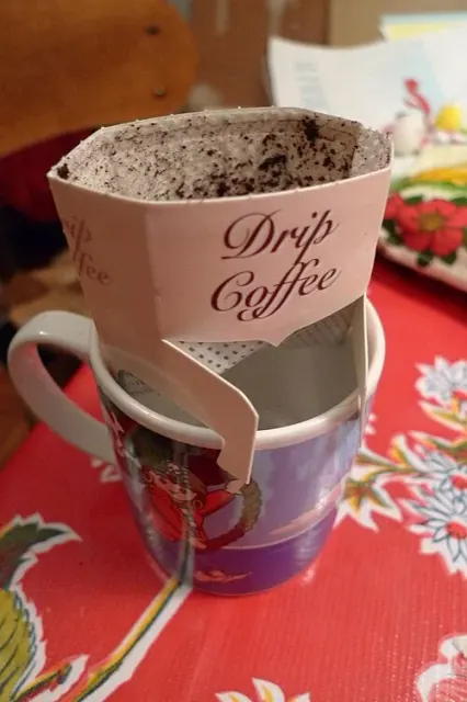 Benutzter Kaffee-Portionsfilter mit Papphaltern auf einer bedruckten Tasse.