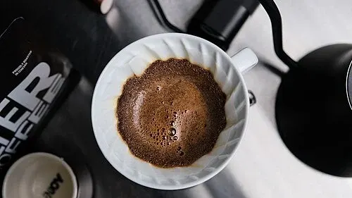 Blick von oben auf einen V60-Handfilter mit weißem Papier und frisch aufgegossenem Kaffeemehl.