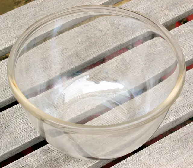 Transparente runde Glasschüssel mit breitem Rand auf hellen Holzlatten