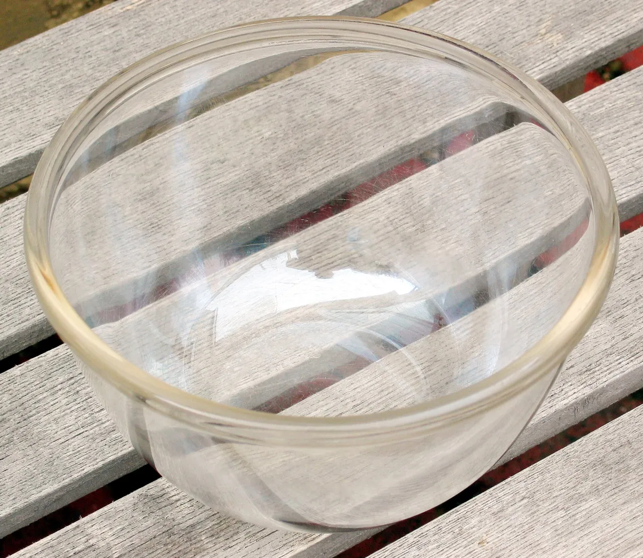 Transparente runde Glasschüssel mit breitem Rand auf hellen Holzlatten