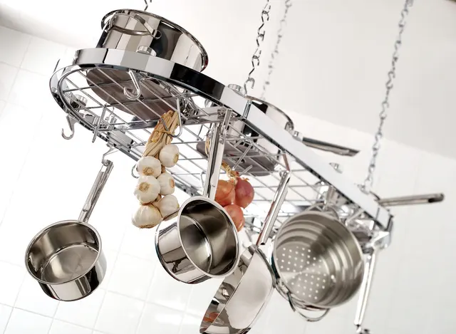 Mehrere Töpfe, Pfannen und ein Sieb hängen an einem Metallgestell unter der Decke