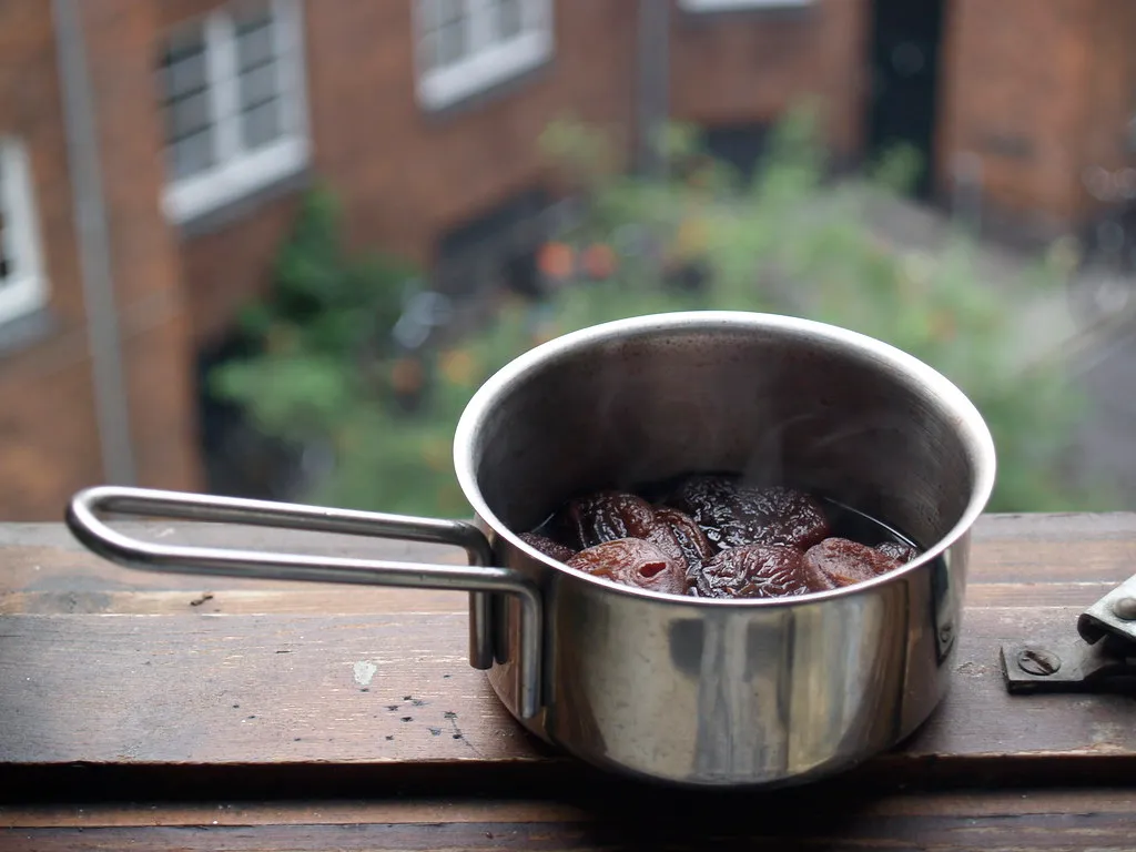 Kleiner Edelstahltopf mit Früchten in dunkler Flüssigkeit auf einer Fensterbank