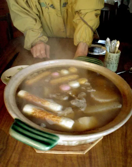 Großes rundes Kochgefäß mit Oden und einer Schöpfkelle auf einem Holztisch