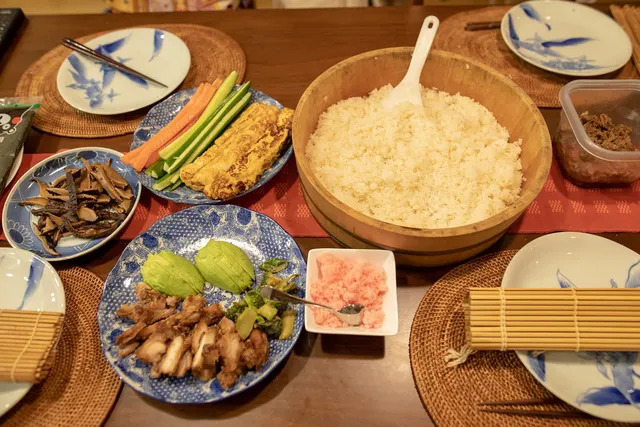 Holzschale mit Sushi-Reis, Reislöffel und Bambusmatten auf einem gedeckten Tisch