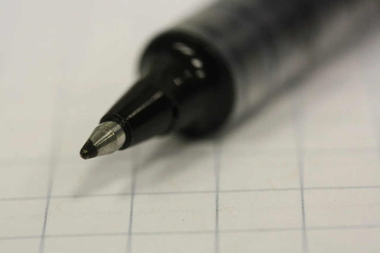 Primer plano de la punta de un bolígrafo Uni-ball sobre papel cuadriculado.