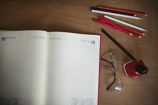 Agenda abierta, lápices, gafas y tinta sobre una mesa.