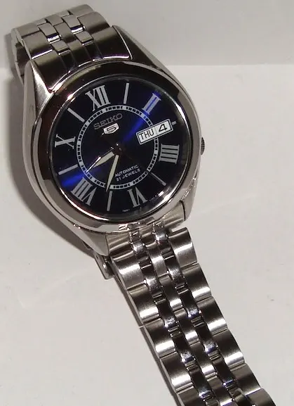 Seiko 5 de esfera azul, números romanos y brazalete metálico.