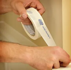 Una persona desenrolla cinta Trimaco Kleenedge para pintura.