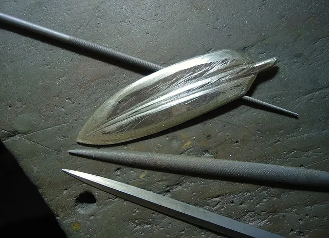 Una pieza metálica con forma de pluma junto a limas de joyería.
