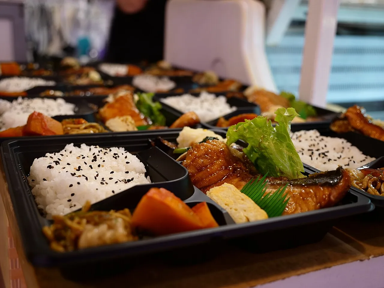Bento en bandeja con compartimentos, arroz y varios acompañamientos.