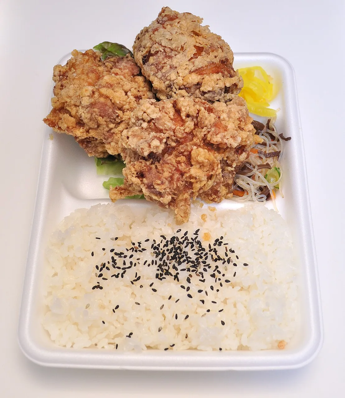 Bento con arroz y piezas empanadas en una bandeja blanca.