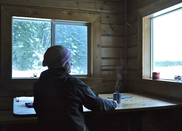 Bebida caliente en una taza metálica Snow Peak dentro de una cabaña de camping. El modelo exacto y el tipo de pared no están identificados; no se presenta como una Ti-Single 450.