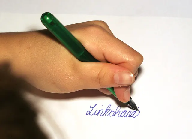 Une main gauche écrit au stylo-plume sur une feuille blanche