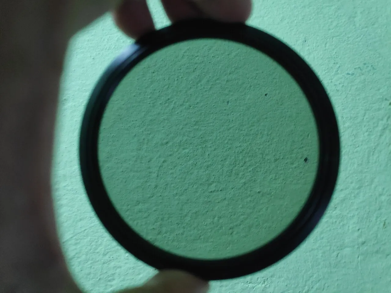 Filtre ND circulaire tenu devant un mur clair