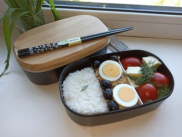 Boîte à bento remplie de riz, d’œufs et de légumes, avec couvercle à côté