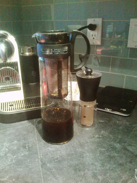 Carafe Hario pour café froid avec son filtre cylindrique, près d’un moulin