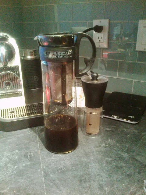 Carafe Hario pour café froid avec son filtre cylindrique, près d’un moulin