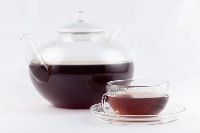 Théière et tasse en verre remplies de thé sur un fond clair