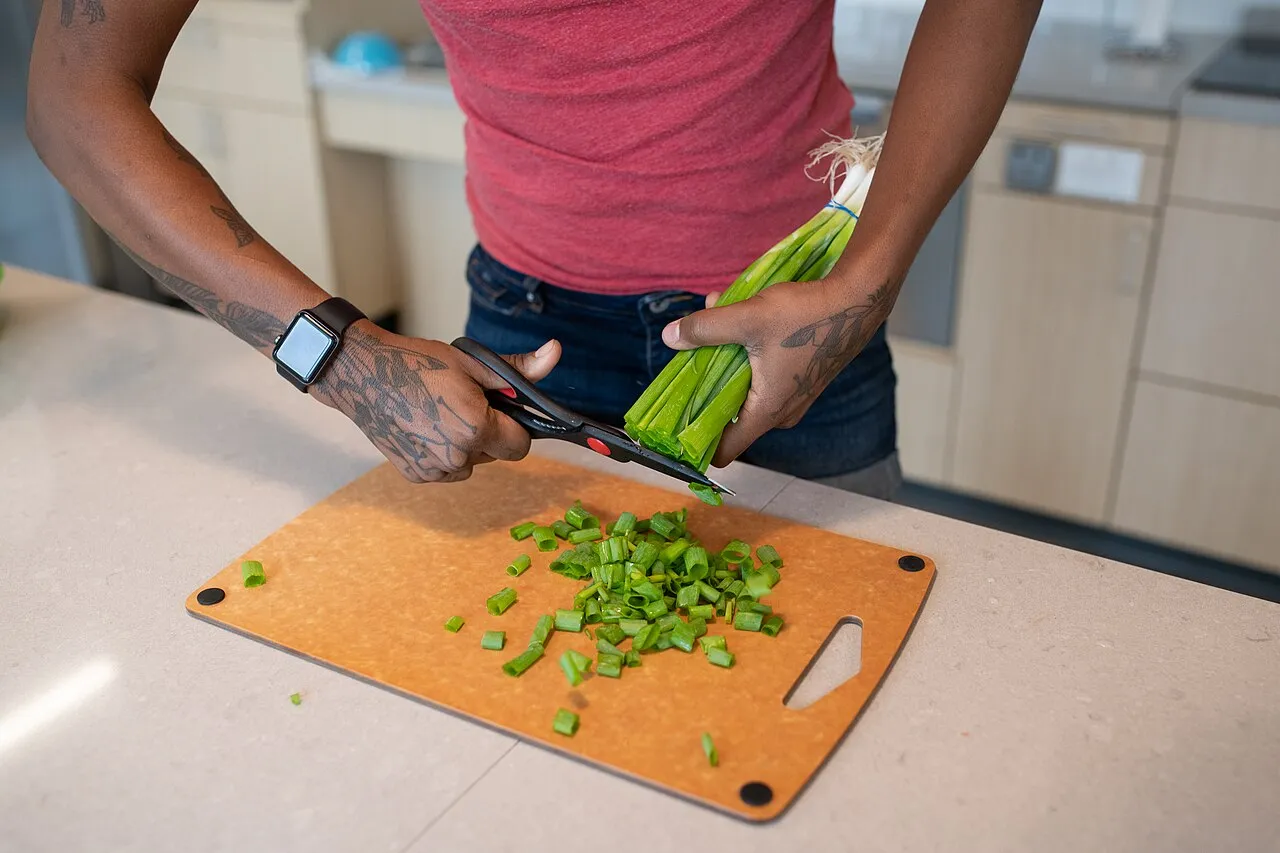 Une personne coupe des oignons verts avec des ciseaux sur une planche