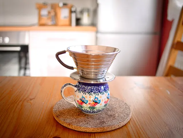 Kalita Wave en acier posé sur une tasse décorée, sur une table en bois