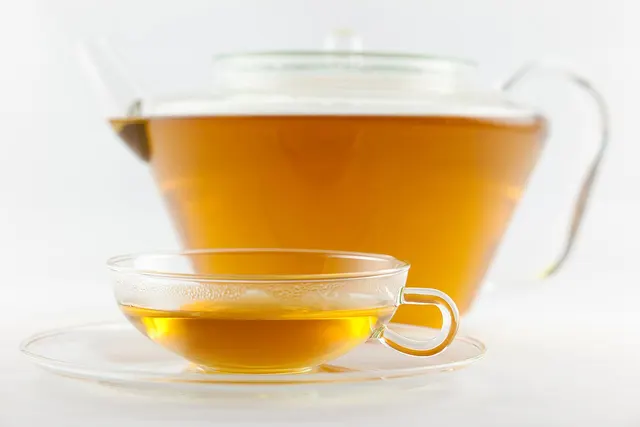 Tasse à thé en verre avec anse et soucoupe, devant une théière