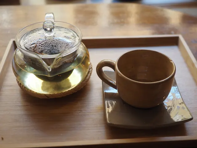 Théière en verre contenant du thé vert et tasse en céramique sur un plateau