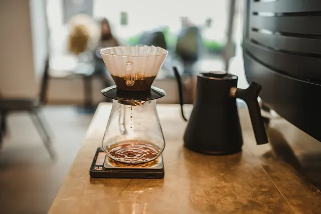 V60, carafe, balance et bouilloire noire réunis sur un comptoir