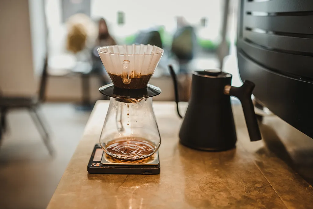 V60, carafe, balance et bouilloire noire réunis sur un comptoir