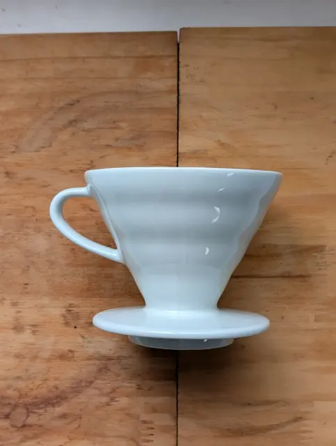 Weißer Hario-V60-Handfilter aus Keramik auf einer Holzfläche.
