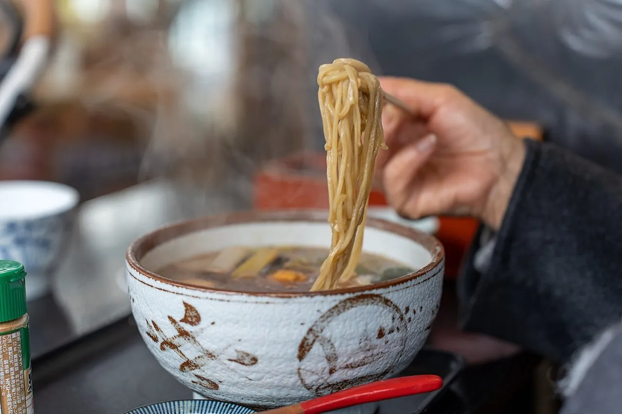Una mano solleva gli udon da una ciotola con le bacchette