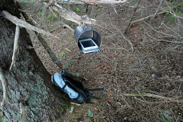 Tazza Snow Peak in titanio appesa a un ramo, con un telefono all’interno
