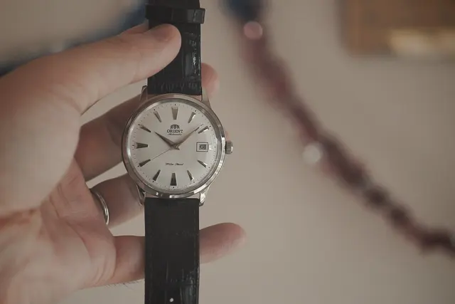 Orient Bambino FER24005W0 med ljus urtavla och svart läderband, hållen i handen.