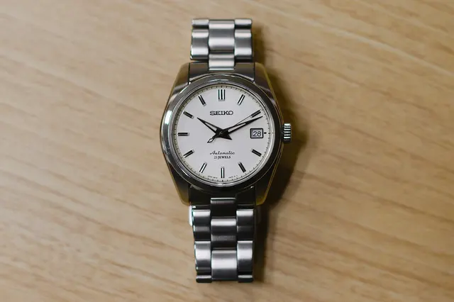 Seiko 5 med ljus urtavla och stållänk på ett träbord.