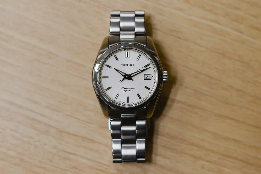 Seiko 5 med ljus urtavla och stållänk på ett träbord.