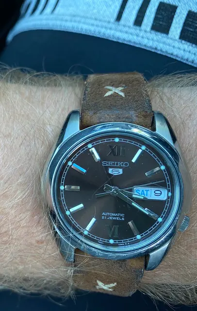Äldre Seiko 5 med mörk urtavla och brunt läderband på en handled.