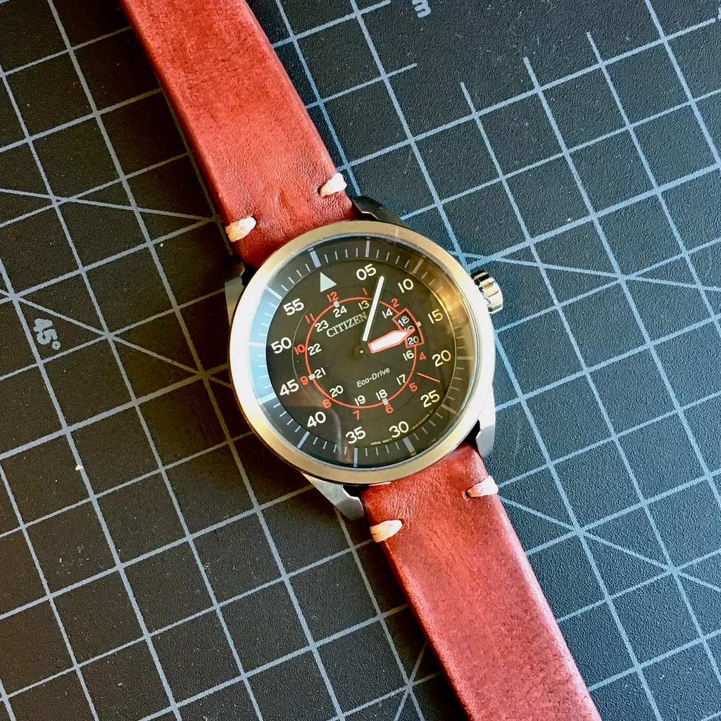 Armbandsur med rött läderband på en rutad skärmatta.