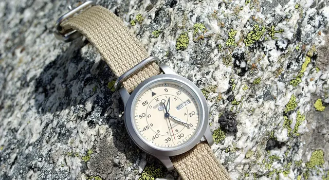 Seiko 5 med ljus urtavla och beigt textilband på en sten.