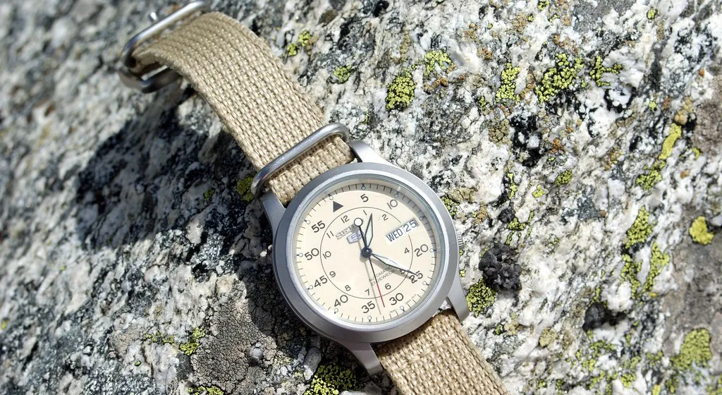 Seiko 5 med ljus urtavla och beigt textilband på en sten.
