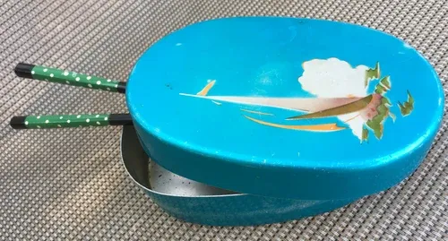 Turkos oval bentolåda med dekorerat lock och ätpinnar.